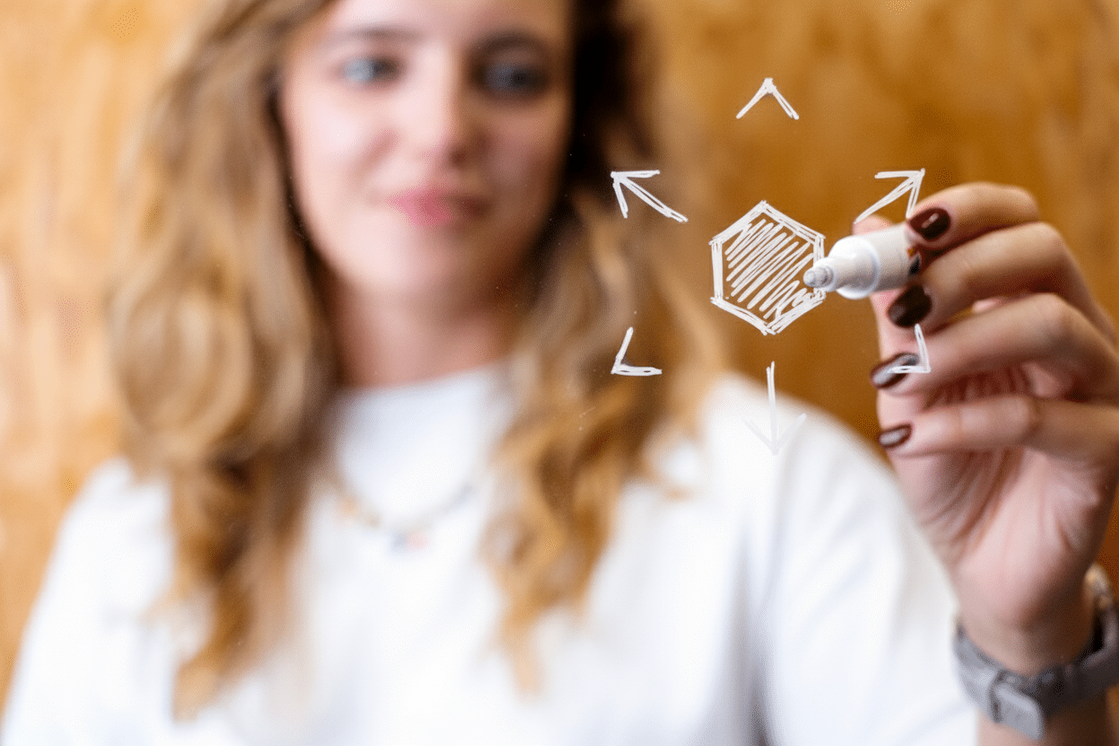 Vrouw tekent een zeshoek met pijlen op glas, symbool voor ideeën of richting.